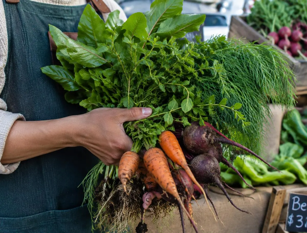 Hands holding fresh greens, carrots, and beets at a market stall